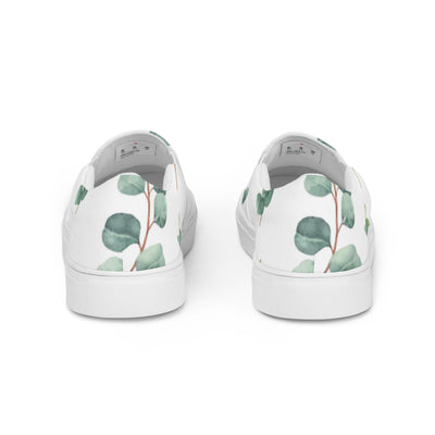 White slip-on canvas shoes with a eucalyptus leaf pattern in green tones, featuring Cachy’s Urban branding on the insoles
