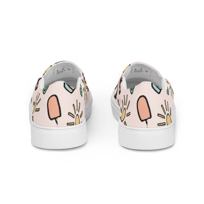 Pink slip-on canvas shoes with playful summer icons featuring suns, sunglasses, and shovels in a cartoon style