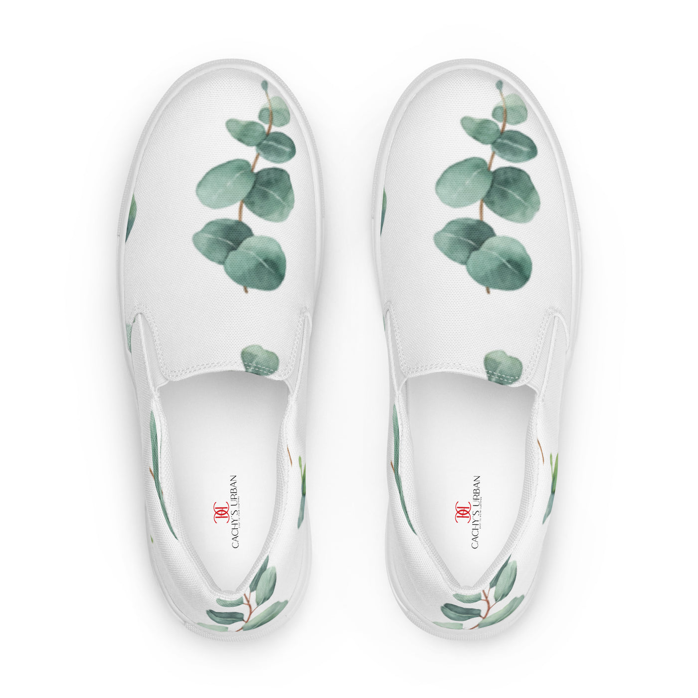 White slip-on canvas shoes with a eucalyptus leaf pattern in green tones, featuring Cachy’s Urban branding on the insoles