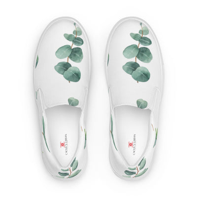 White slip-on canvas shoes with a eucalyptus leaf pattern in green tones, featuring Cachy’s Urban branding on the insoles