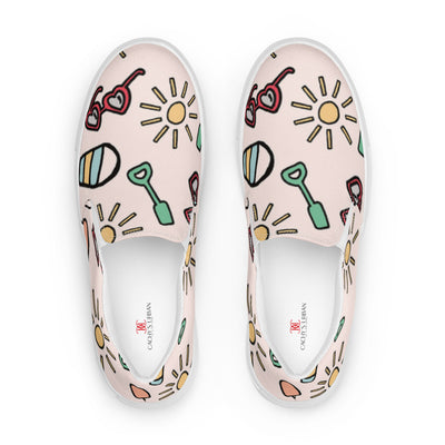 Pink slip-on canvas shoes with playful summer icons featuring suns, sunglasses, and shovels in a cartoon style