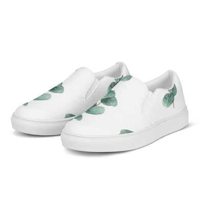 White slip-on canvas shoes with a eucalyptus leaf pattern in green tones, featuring Cachy’s Urban branding on the insoles