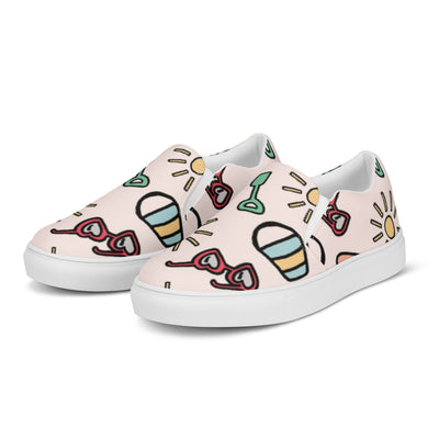 Pink slip-on canvas shoes with playful summer icons featuring suns, sunglasses, and shovels in a cartoon style